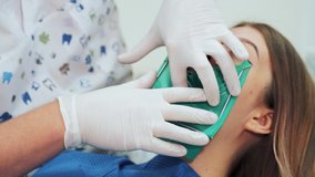 A dentist in white latex gloves makes a green rubber dam with a metal frame. Beginning of a treatment procedure in a dental clinic.