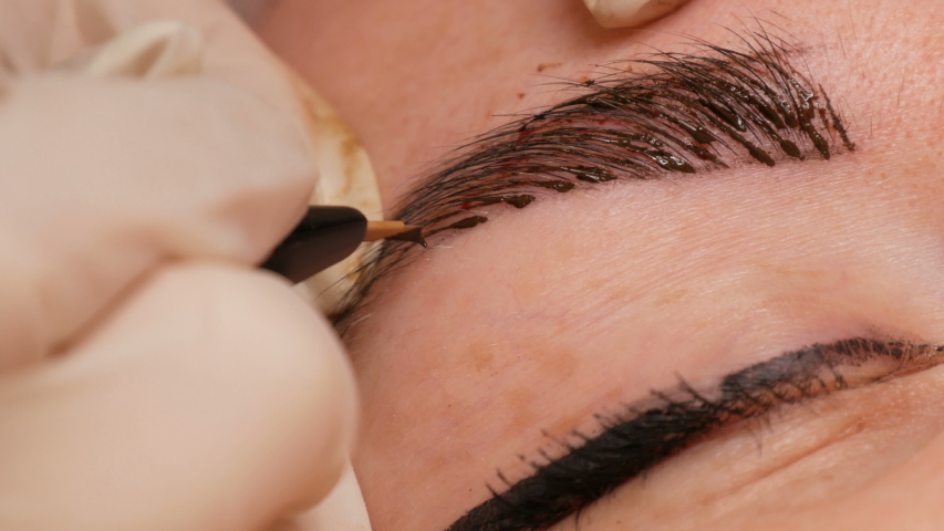 Microblading eyebrow tattoo, permanent makeup. A master in gloves, using special needle, injects pigment into the skin and stains the eyebrows using hair technique, making them natural, close-up view Royalty-Free Stock Footage #1041489724