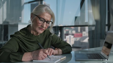 Office Work of Beautiful Elderly Woman. Grey-Haired Businesswoman in Glass Interior of Briefing Room. Matured Banking Person in Glasses at Job Thinks about Leadership Success and Business Solutions