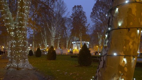 CLOSE UP: White Christmas lights turn the park in downtown Zagreb into a gorgeous winter wonderland. People walk around the scenic Christmas village in Croatia. Picturesque advent market and park.