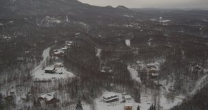 Aerial helicopter shot, above small, rural, snowy Alaskan town, tilt down to see cabins amongst snow and woods, hillside, drone footage