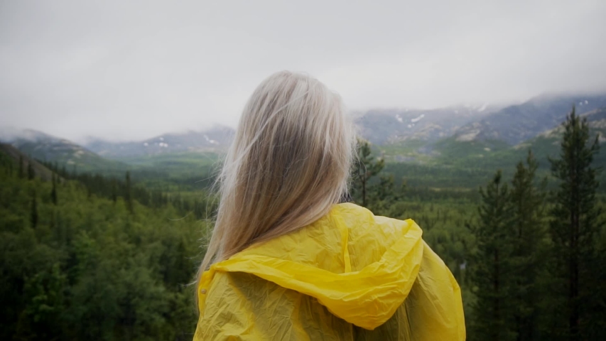 Back view of girl standing on the rock and looking at horizon with mountains. Vacation, travel and adventure concept