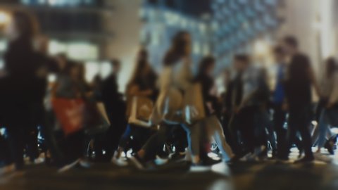 Shoppers and pedestrians on the street carry shopping handbags and cross the busy city intersection at night during the Black Friday week. Blurred