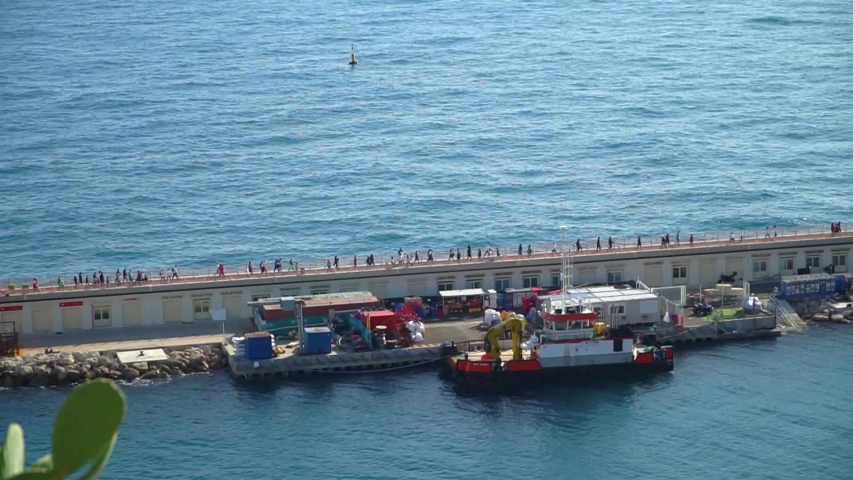 A crowd of people walking on a bridge or wall in the seaport of Monaco Monte Carlo. Moored ships in the port. 