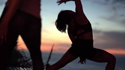 Yoga instructor transitions from warrior 2 to triangle pose in front of beautiful sunset in the distance