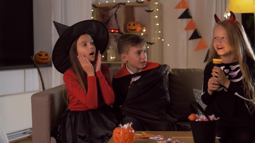 halloween, holiday and childhood concept - smiling boy and girls in costumes playing with flashlight and scaring each other at home