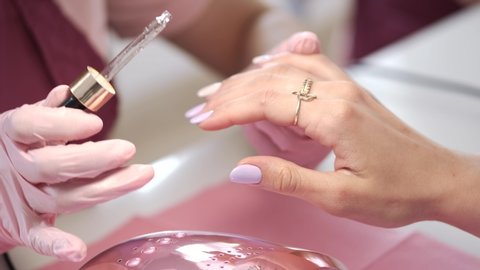 A manicurist wears the pink gloves. A table is white. The girl uses nail strip.