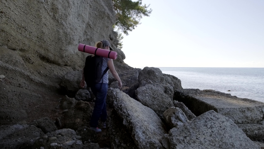 Woman traveler climbs stones and looks at sea. female tourist walks along rocky shore of sea near mountain.
