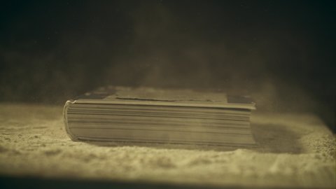 Super slow motion shot of a book falling down on a dusty wooden table, close-up