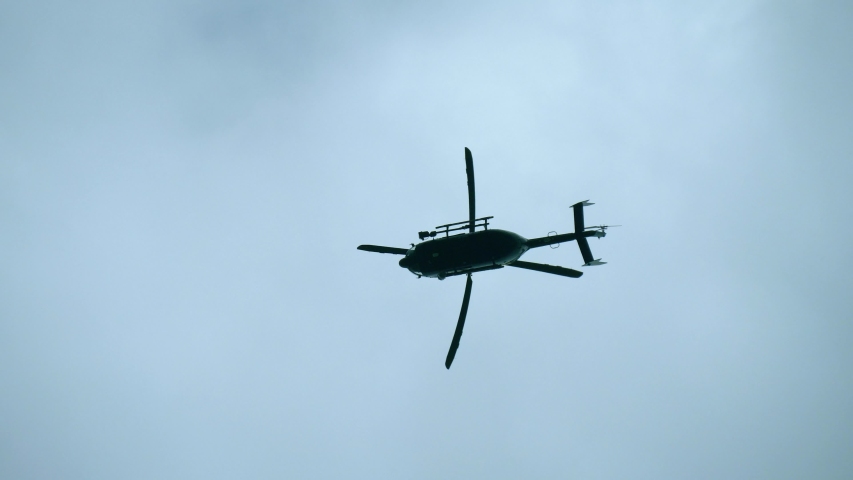A modern, black helicopter hovers in the sky, as viewed from the bottom up. Silhouette of a modern helicopter hovering in the sky, the blades spin slowly.