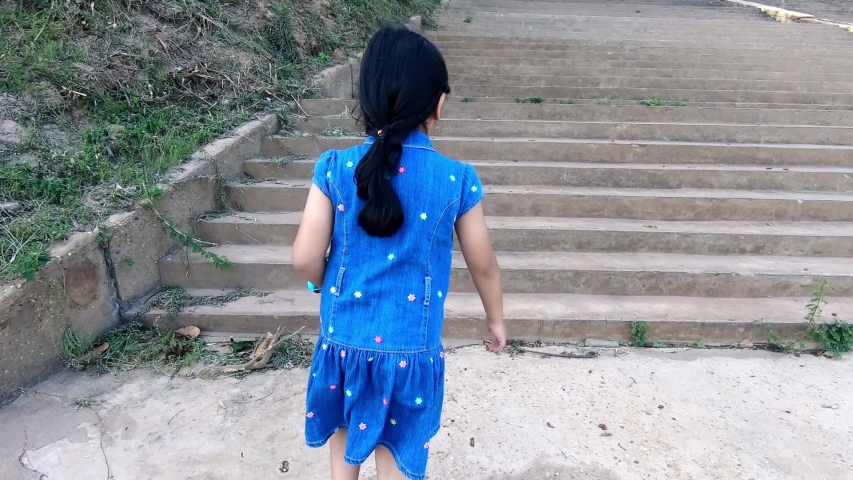 An Asian girl is walking up the cement steps one step at a time