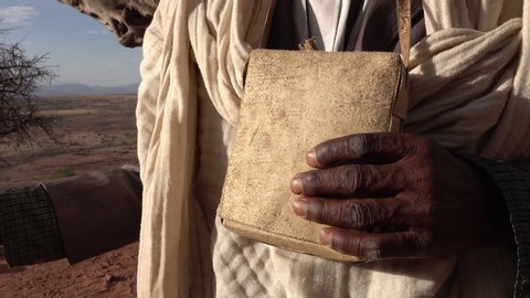 TIGRAY, ETHIOPIA – MARCH 2019: Senior priest holds leather pouch in remote mountainous desert location in Tigray region of Ethiopia