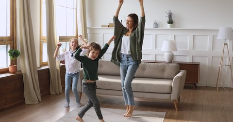 Happy family young adult single mother babysitter and funny small kids having fun jump dance at home, cute little children son daughter enjoy positive emotions active lifestyle in modern living room