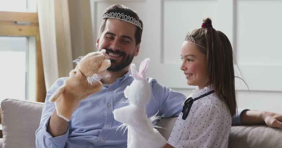 Funny happy young adult dad laughing wearing crown playing puppet toys theater with cute small kid daughter sit on sofa, cheerful loving father enjoying game having fun with little child girl at home Royalty-Free Stock Footage #1041538648