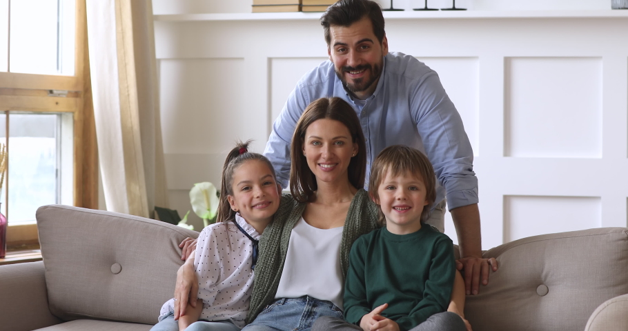 Happy family of four portrait, young adult foster parents mother and father bonding with funny cute school children kids son daughter laughing look at camera posing together on couch in modern home Royalty-Free Stock Footage #1041538693