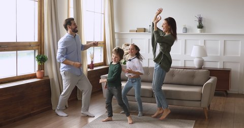Crazy happy family young adult parents mum dad and cute funny active little children kids listening music dancing jumping together having fun in modern living room enjoying leisure lifestyle at home