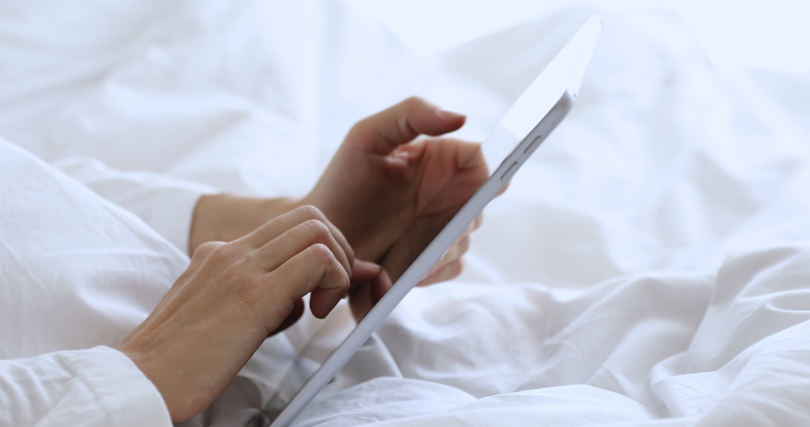 Woman wear pajama holding in female hands using digital tablet computer gadget browsing social media apps, doing online shopping in internet on touchscreen device concept in bedroom, close up view