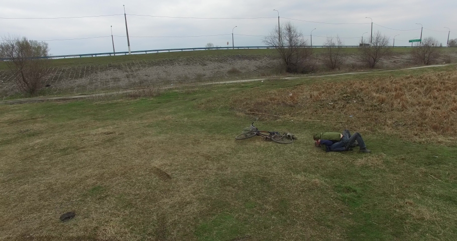 Aerial drone flight view of drunk dirty  men fight on riverbank shore while fishing in countryside in Ukraine. Adults hug lie unconscious on green grass. Village atmosphere mood