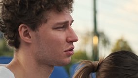 Close up view of Pleased curly male tennis player talking and having rest together with his happy female opponent on tennis court