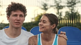 Pleased curly male tennis player talking and having rest together with his happy female opponent on tennis court
