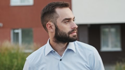 Cool pleased bearded businessman looking at the camera and posing outdoors