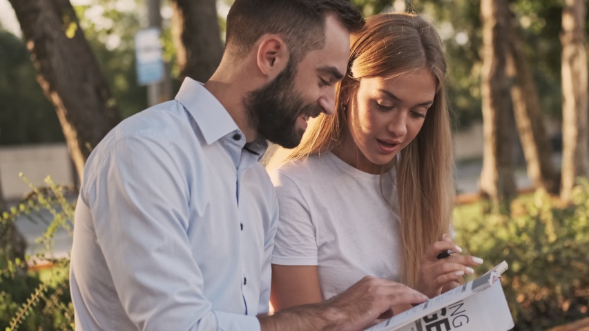 Happy young office colleagues studying with magazine and writing something in notebook outdoors