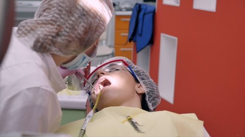 Woman Dentist Treating Teeth to Woman Patient in Clinic. Oral hygiene with a special solution, cleaning the oral cavity with ultra sound. Female professional dentist doctor at work. Dental examination