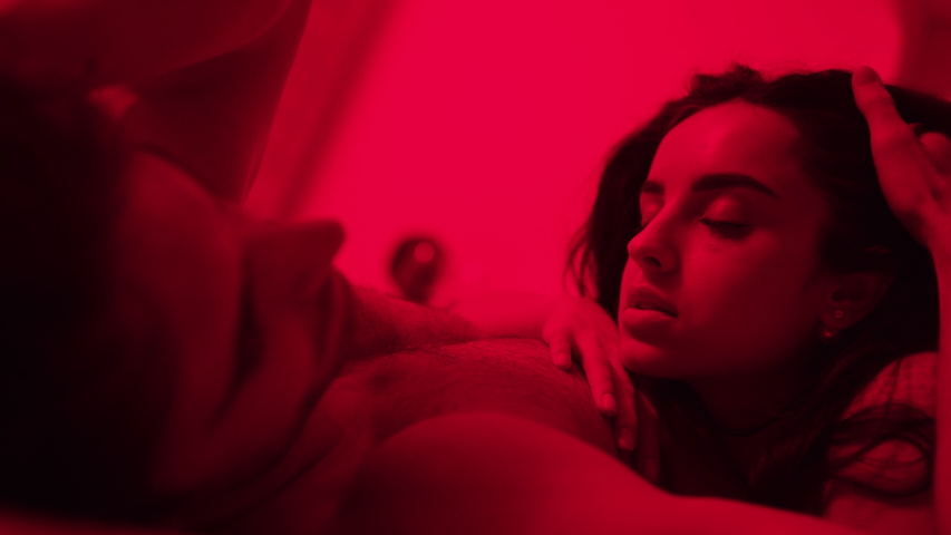 Sexy couple hugging on bed at night time in slow motion. Close up of naked lovers resting in bed after sex in red light. Young woman looking on boyfriend tenderly. Intimate moment.