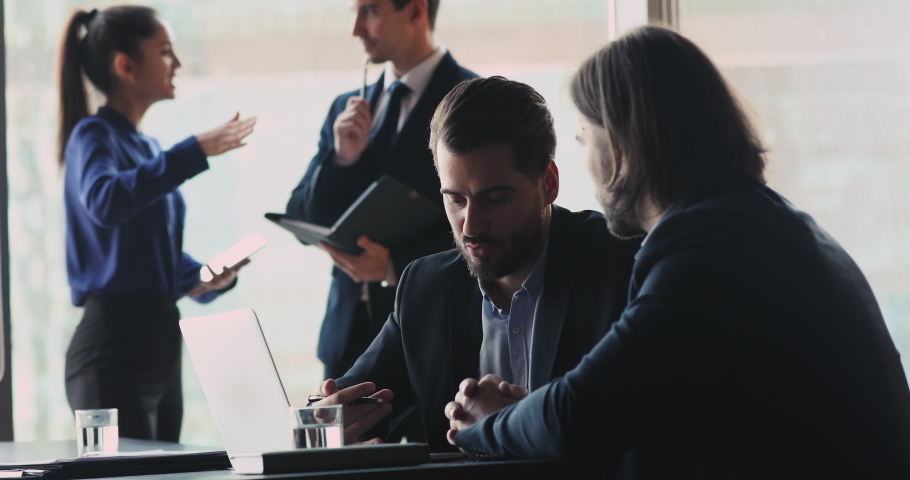 Serious businessman wear suit speaking to male colleague partner investor explaining strategy plan with laptop sit at meeting table, two professional businessmen talking in modern corporate office Royalty-Free Stock Footage #1041547702