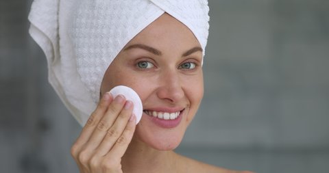 Healthy happy beautiful young lady with towel on head cleaning purifying facial skin care hold cleansing sponge look at camera, smiling woman remove makeup with cleanser, skincare treatment concept