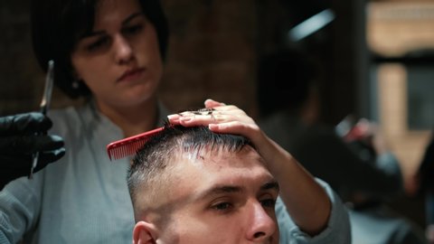 Barber cuts the hair of the client with scissors close-up. Frame. Barber combing hair and cutting with hairdressing scissors.