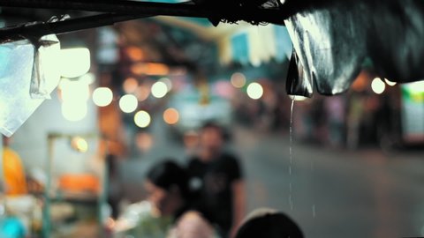 Water dripping of the top of a street food vendor tarp roof. Dripping water is in focus with bangkok food vendors and traffic in the background, nice smooth panning.