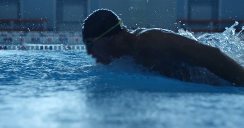 A professional swimmer raising a lot of splashes is swimming in butterfly style along his path in the pool. Slow mo, slo mo, slow motion, high speed camera