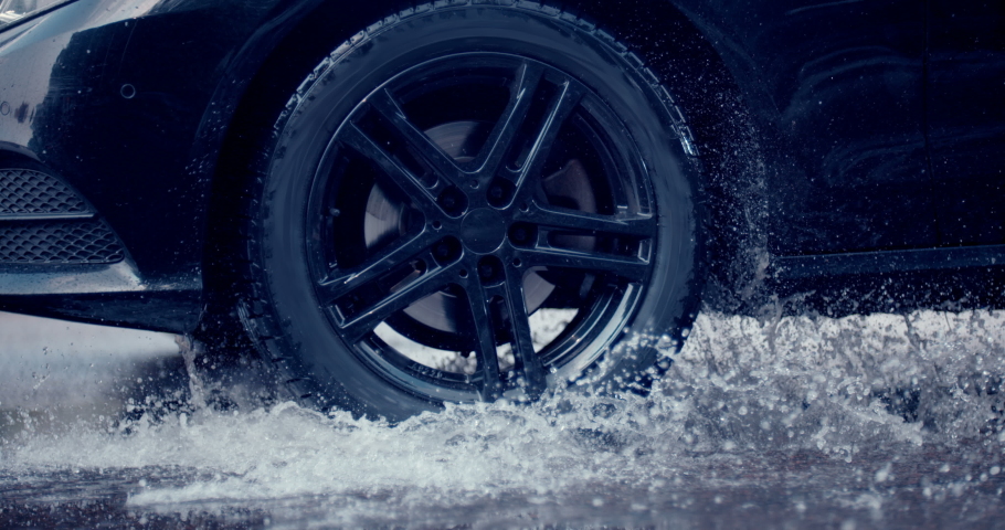 Reflecting everything around with its glossy surface, the premium car rides in extreme conditions - on a puddle on the road, where a large stream of spray erupts from under the wheels | Shutterstock HD Video #1041554272