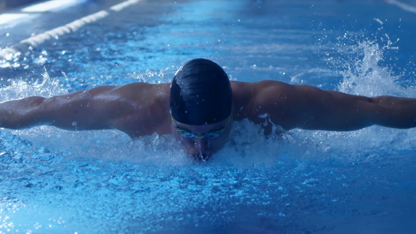 A professional swimmer raising a lot of splashes is swimming in butterfly style along his path in the pool. Slow mo, slo mo, slow motion, high speed camera Royalty-Free Stock Footage #1041563776