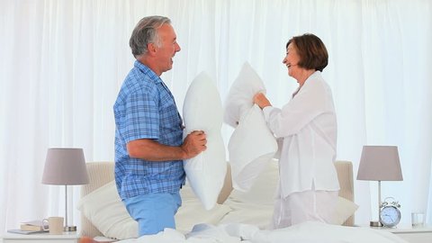 Retired Caucasian couple playing with pillows on the bed
