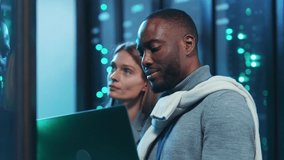 Diverse team of IT engineers discussing work issues using laptop in server room. Chief administrator with server assistant coworking and talking in data center cyberspace. - Powered by Shutterstock - Get 15% off with code: PIKWIZARD15