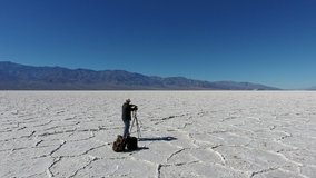 Skilled male photographer standing near camera and tripod shooting video of beautiful salt desert on horizon, hipster guy making photos during journey to death valley with equipment