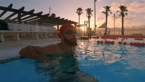 Professional muscular swimmer relaxing after his training in the olympic swimming pool at the sunrise. Slow motion 4k (UHD).