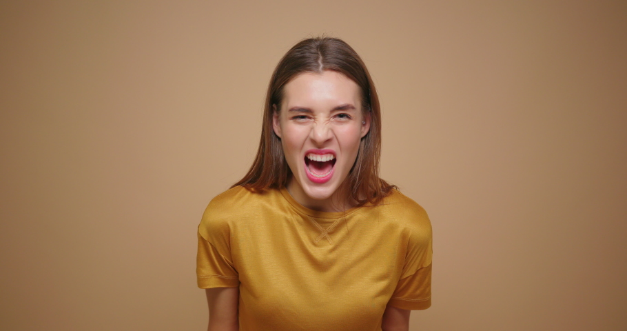 Close up of a young stressed woman screaming loud in yellow t shirt shout loud isolated on beige background. | Shutterstock HD Video #1041583045