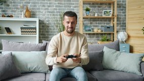 Portrait of cheerful carefree guy playing computer game in house alone looking at camera holding joystick having fun. Lifestyle and entertainment concept.