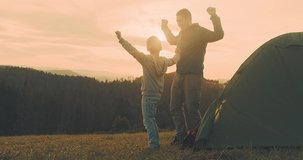 Happy traveler father and son playing, bonding near tent camp around mountain under sun light enjoying the leisure and freedom. 4K slow motion video

