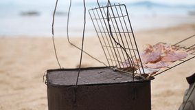 Old grungy do-it-yourself portable charcoal stove, street wise, being used to grill dry squid for sale at a beachside in Thailand