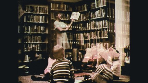 1970s: woman reading book aloud to children, children looking at a book together