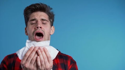 Young man sneezes into tissue. Isolated guy is sick, has a cold or allergic reaction. Coronavirus, epidemic 2020, illness concept.