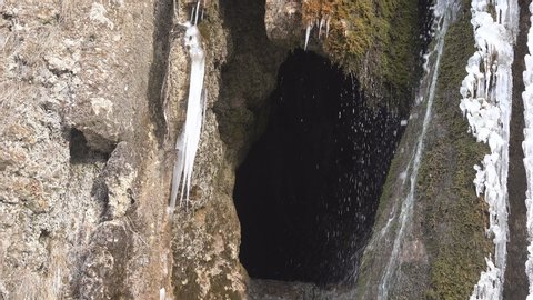 Spring. At entrance to rock dwelling water flows down, icicles froze. Caveman enters, troglodyte dwelling. In such shelter mountaineers were saved at attack of enemy (easier to protect). Caucasus