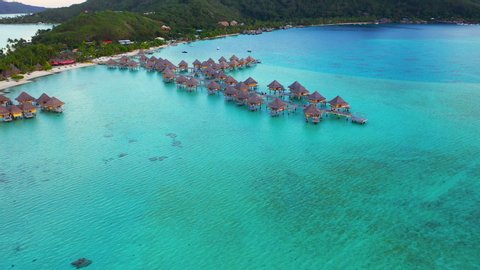 Aerial of charming overwater bungalows in a beautiful blue lagoon, drone flying forward then tilting down showing top view of the bungalows - Bora Bora, French Polynesia