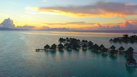 Aerial of charming overwater bungalows on a beautiful tropical beach at sunset, drone flying forward then tilting down over the bungalows and ascending - Bora Bora, French Polynesia