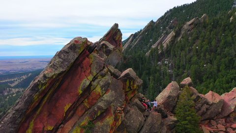 Aerial: Drone reversing over friends standing on rocky mountain peak, scenic view of landscape against sky - Boulder, Colorado