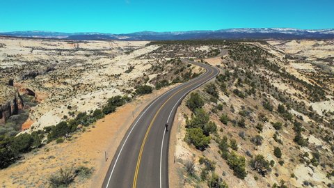 Aerial: Man skateboarding on highway at Grand Staircase-Escalante National Monument, road amidst bushes in desert on sunny day